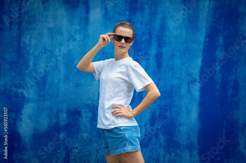Female model wearing white blank t-shirt on the background of an blue wall.