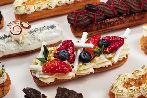 Elegant éclairs dressed with whipped cream and a colorful array of fresh fruit, presenting a tempting treat for dessert connoisseurs.
