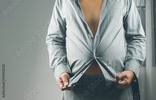 people, businessman, fashion and clothing concept of fat man dressing up. Man trying to button a small shirt.