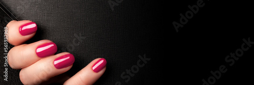 Female hand with beautiful manicure - viva magenta, pink nails on black leather surface background banner with copy space. Wide panoramic header