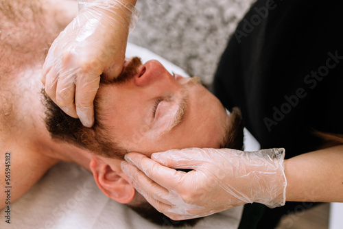 Man receiving facial buccal massage in beauty salon.Beauty and skincare concept with a beautiful woman. Middle aged male relaxed with massage for facial lifting