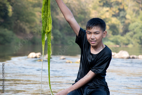 Asian schoolboy holding freshwater algae from diving into the river and pulling it up to study the fertility of the river's nature and to do environment school project work, in motion. photo