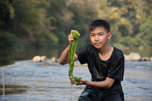 Asian schoolboy holding freshwater algae from diving into the river and pulling it up to study the fertility of the river's nature and to do environment school project work, in motion. photo