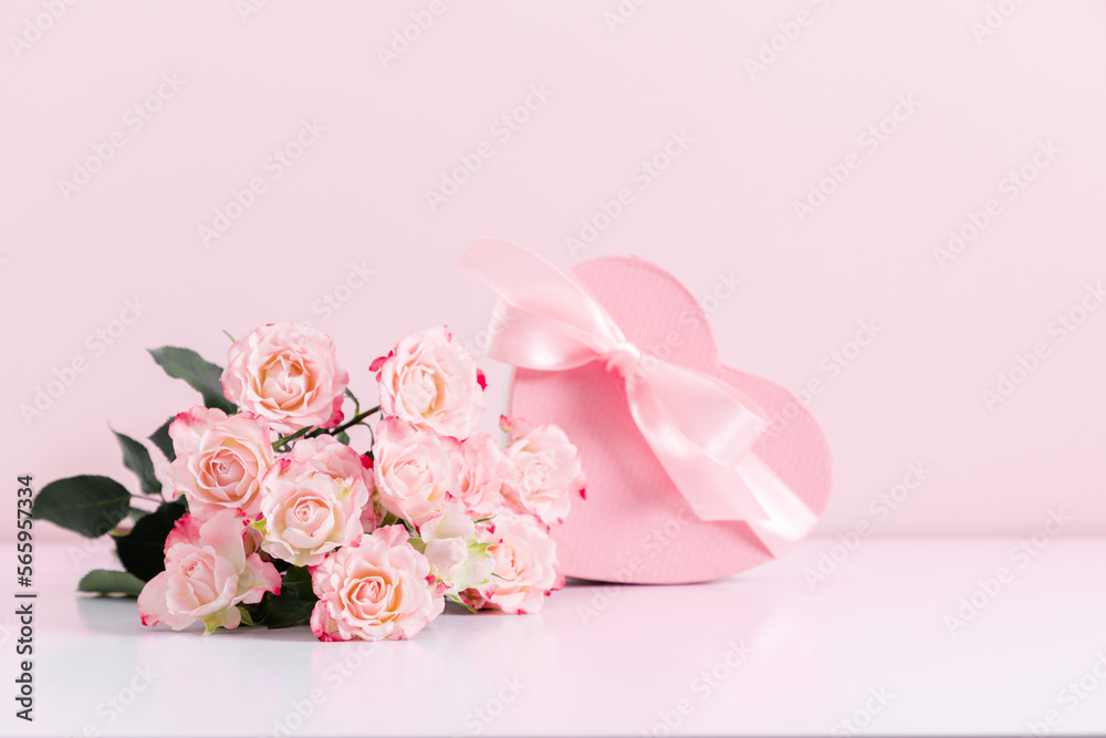 Bouquet of pink rose flowers and heart shaped gift box with satin bow on pastel pink table background. Birthday, Wedding, Mother's Day, Valentine's day, Women's Day. Front view