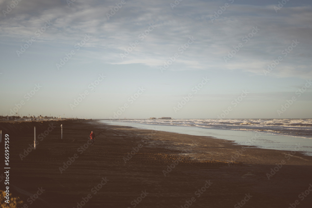 Spiaggia deserta di Rimini durante una giornata invernale con mare agitato, in lontananza piccola presenza umana.