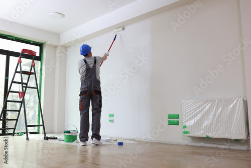 Professional painter paints office wall with roller brush.