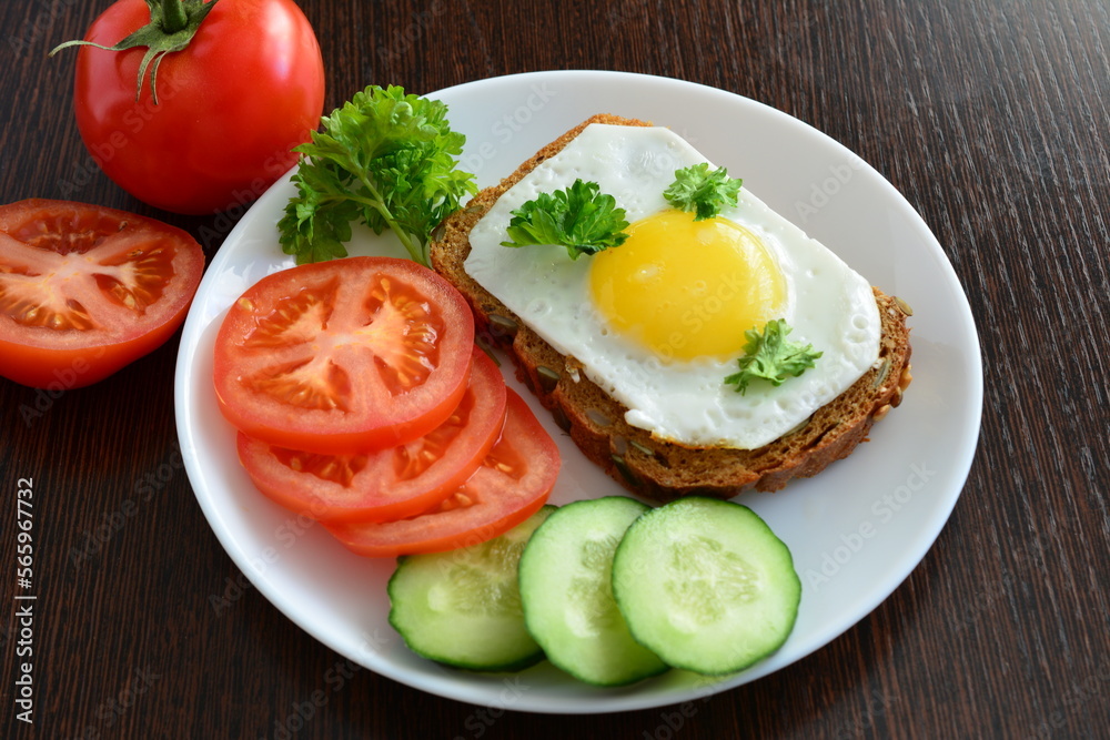 healthy sandwich with fried egg with yellow yolk on white plate with sliced vegetables healthy sandwich with fried egg with yellow yolk on white plate with sliced vegetables