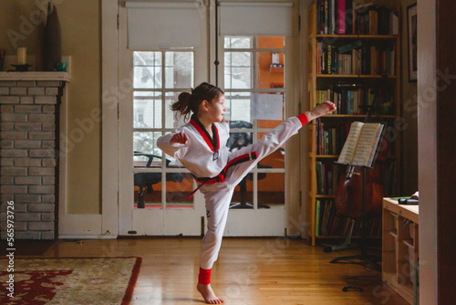 A young girl does Taekwondo kick in uniform at home photo