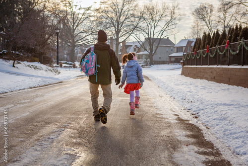 Rear-view of father and daughter walking to school on snowy street photo