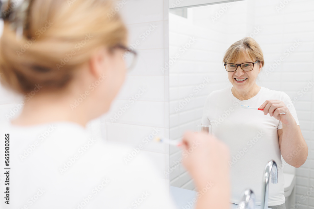 Obraz premium Happy caucasian woman brushing teeth and looking at mirror in bathroom