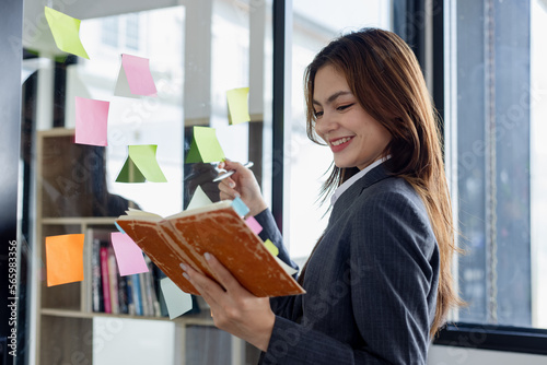 Young business woman working with paper note on glass wall, Business people meeting to share idea at office, Business planning and Sticky note on glass wall.