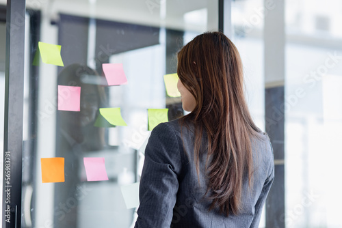 Young business woman working with paper note on glass wall, Business people meeting to share idea at office, Business planning and Sticky note on glass wall.