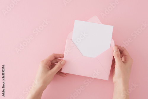 Women day concept. First person top view photo of female hands holding open pink envelope with white card over pastel pink background with copy space. Mother's day minimal idea.