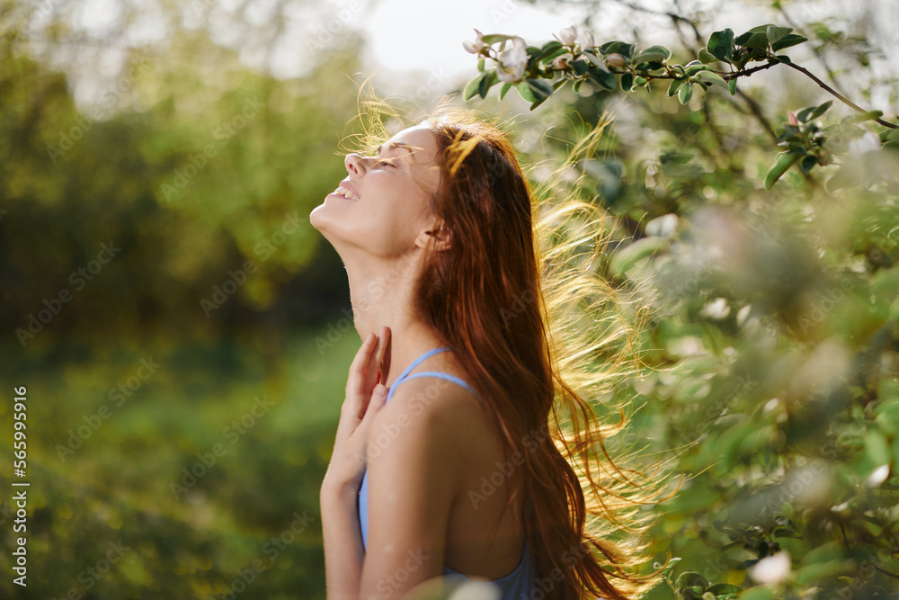 Woman with a beautiful smile with teeth and long hair in the spring sunset in nature in the park near the flowering trees happiness, natural beauty and hair health Woman with a beautiful smile with teeth and long hair in the spring sunset in nature in the park near the flowering trees happiness, natural beauty and hair health