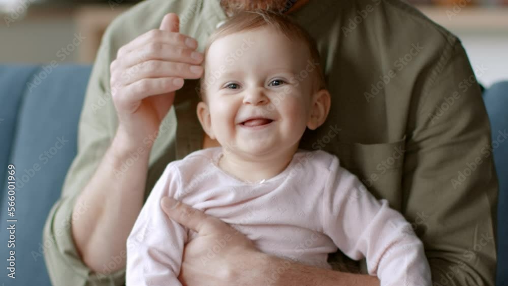 Happy family. Close up portrait of adorable little baby girl laughing to camera, unrecognizable daddy embracing his girl