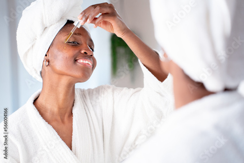 Young woman applying serum in pippette dropper on cheek, natural oil skin beauty treatment bathroom