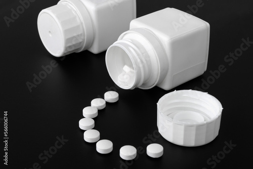 White pills spilled from a pill bottle on dark background.