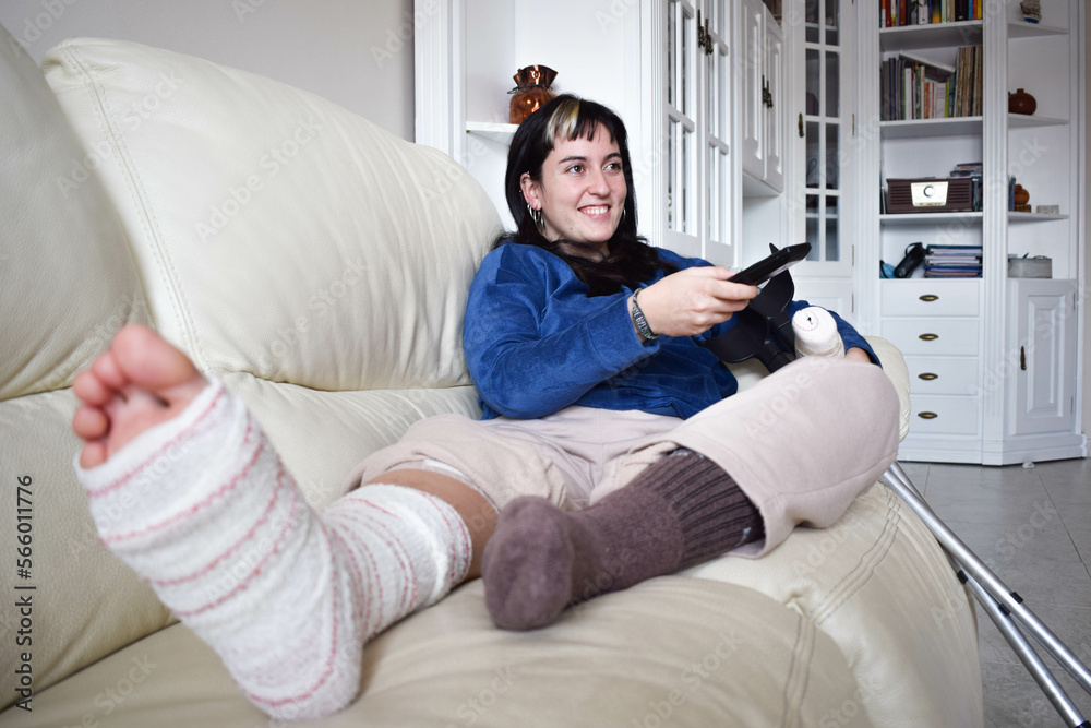 Young woman on couch at home with crutches and orthopedic plaster