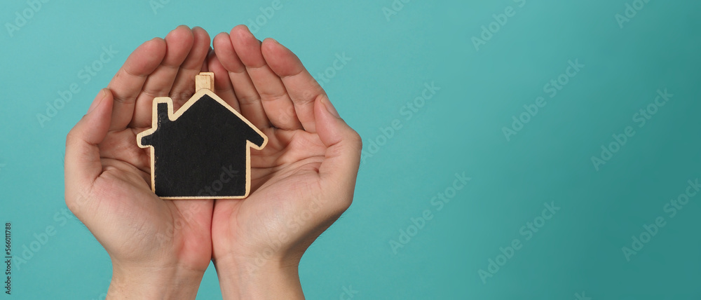 Small wood house in hands represent concepts such as home care family love real estate housing shelter insurance and mortgage. Hands holding small model house isolated on blue green studio background. Small wood house in hands represent concepts such as home care family love real estate housing shelter insurance and mortgage. Hands holding small model house isolated on blue green studio background.
