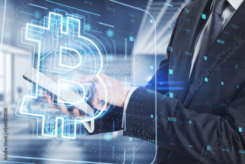 Close up of businessman hands using tablet with glowing bitcoin hologram on blurry office interior background. Mining and trade bitcoin concept. Bitcoin hits new record. Double exposure.