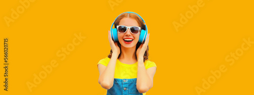 Portrait of happy smiling young woman with headphones listening to music on yellow background