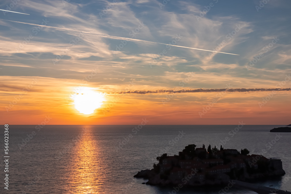 Panoramic sunset view at Adriatic Mediterranean Sea near Sveti Stefan, Budva Riviera, Montenegro, Europe. Reflection of sun beams on water surface during twilight. Summer vacation in seaside resort