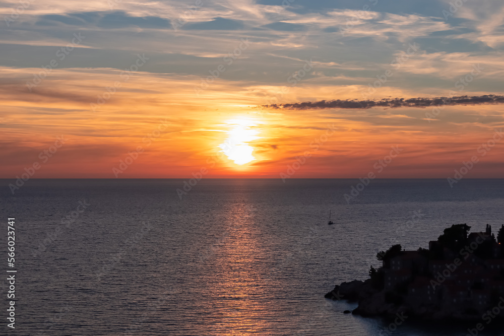Fototapeta premium Panoramic sunset view at Adriatic Mediterranean Sea near Sveti Stefan, Budva Riviera, Montenegro, Europe. Reflection of sun beams on water surface during twilight. Summer vacation in seaside resort