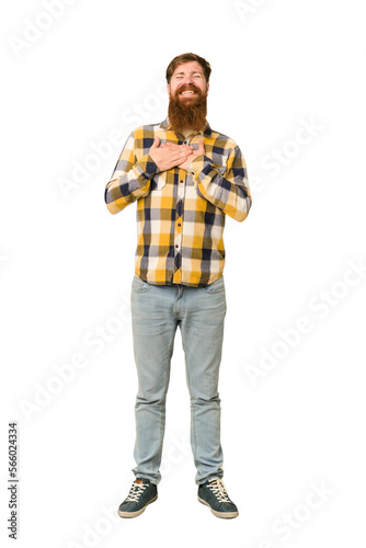 Young adult redhead man with a long beard standing full body isolated laughing keeping hands on heart, concept of happiness.