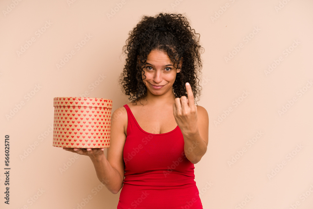 Young african american woman holding a valentines day box gift isolated pointing with finger at you as if inviting come closer. Young african american woman holding a valentines day box gift isolated pointing with finger at you as if inviting come closer.