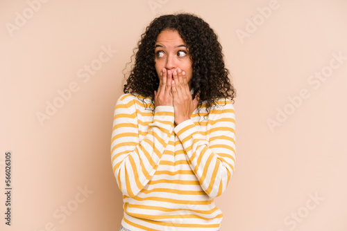 Young african american curly woman isolated thoughtful looking to a copy space covering mouth with hand.
