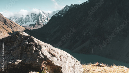 View from the top of Lake Shavlinskoe in the shade between the mountains behind a stone against the backdrop of snowy peaks with glaciers in Altai in the evening.