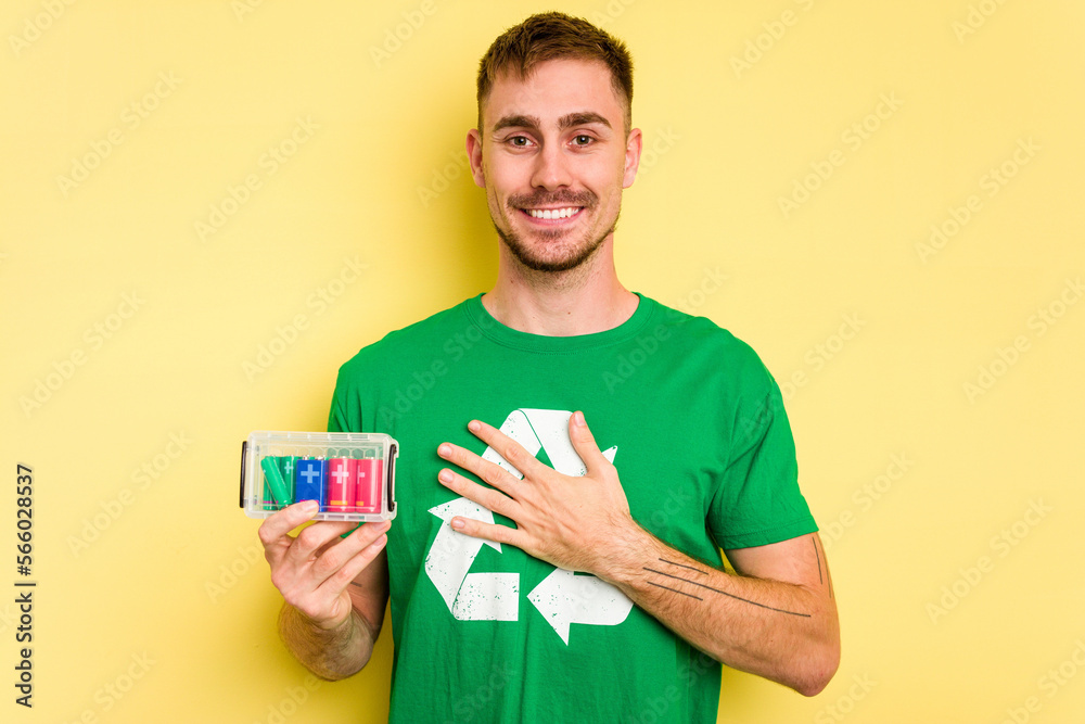 Young man holding batteries to recycle them cut out isolated laughs out loudly keeping hand on chest. Young man holding batteries to recycle them cut out isolated laughs out loudly keeping hand on chest.