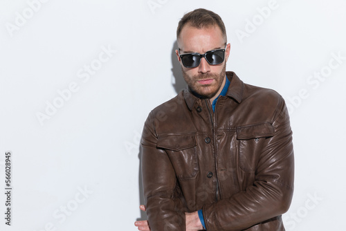 cool fashion guy in brown leather jacket with sunglasses posing