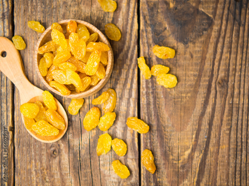 Golden dried raisins in a wooden bowl and spoon on an old wooden table.