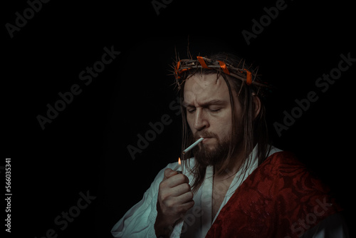 Fotografie Jesus Christ smokes a cigarette wearing a crown of thorns and white chiton toga
