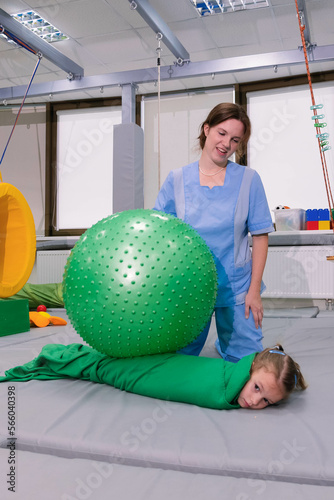 Physical therapist working with little girl in sensory room. Exercising with fitness ball and pressure to help kid relax in a therapy center. sensory integration session