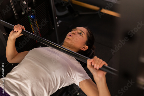 Hispanic young sports woman lifting weights in the gym 