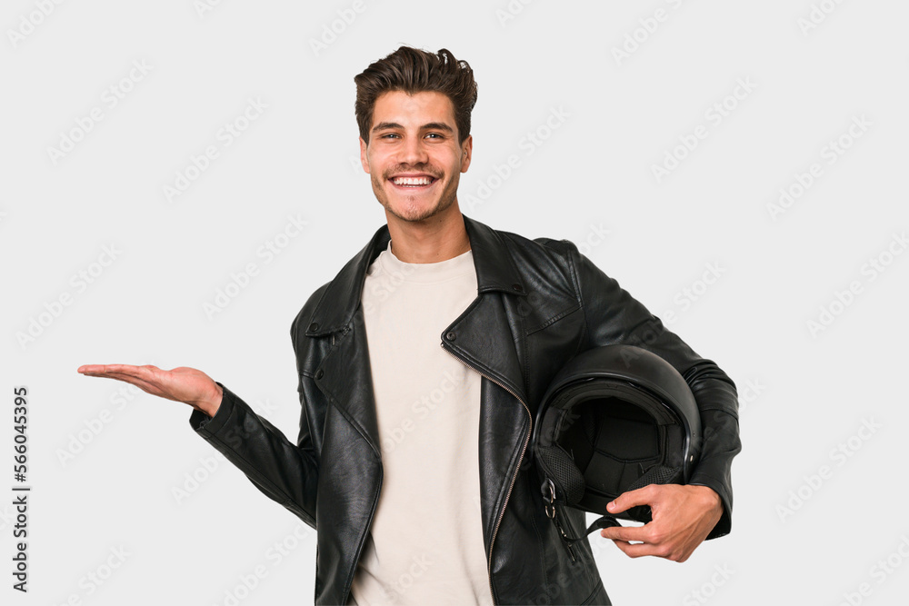 Young caucasian man holding a motrbike black helmet isolated showing a copy space on a palm and holding another hand on waist. Young caucasian man holding a motrbike black helmet isolated showing a copy space on a palm and holding another hand on waist.
