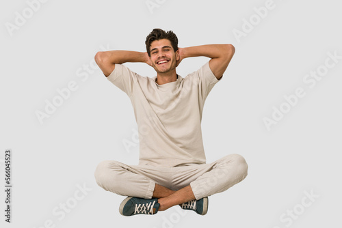 Young caucasian man sitting on the floor isolated on white background stretching arms, relaxed position.