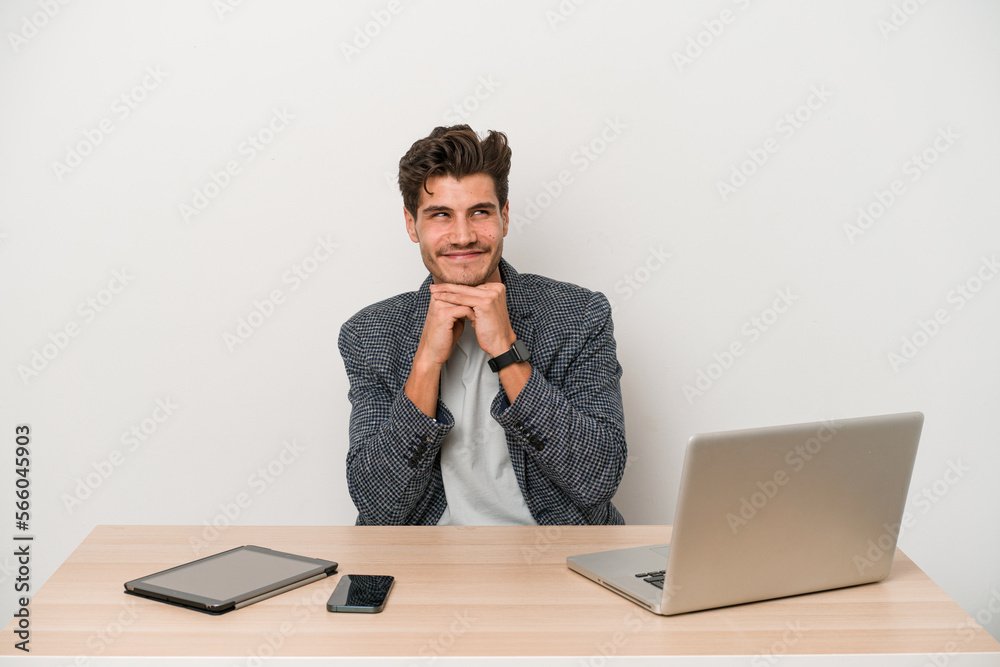 Young entrepreneur man working with a laptop isolated keeps hands under chin, is looking happily aside. Young entrepreneur man working with a laptop isolated keeps hands under chin, is looking happily aside.