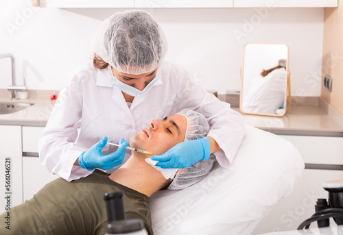 Young man patient of beautician receiving rejuvenating facial injections, concept of male aesthetic skin care