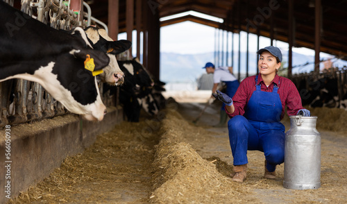 Smiling farmer woman stands in open cowshed and shows cow farm
