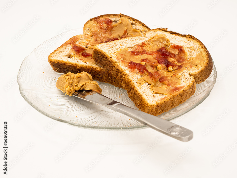 Two classical American sandwiches with peanut butter and jelly on a glass plate with a knife with peanut butter, isolated on white background. Two classical American sandwiches with peanut butter and jelly on a glass plate with a knife with peanut butter, isolated on white background.