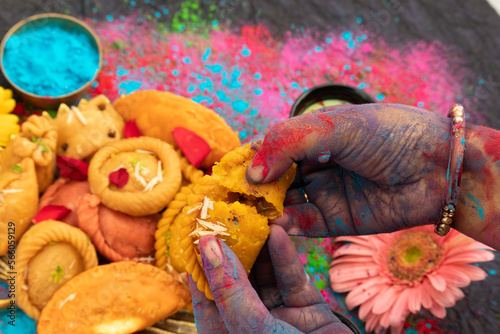 Hands Of A Girl Painted With Colorful Gulal Holding Delicious Gujiya Also Called Gujia, Ghughra, Karanji, Somas, Garijalu, Kajjikayalu, Karigadubu, Gunjiya, Pedakiya, Karjikayi During Holi Celebration photo