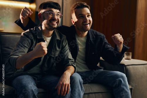 Two men are sitting on the couch at home and watching TV. Great TV show, guys are happy, their team won. The concept of watching sports competitions, football.