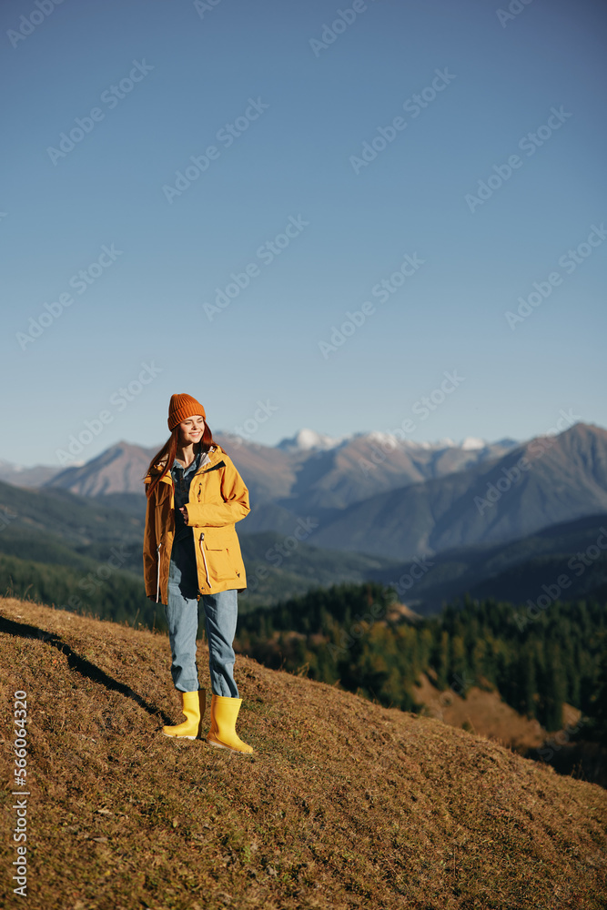 Woman autumn full-length walk on the hill smile with teeth and look at the mountains in a yellow raincoat and jeans happy hiking trip, freedom lifestyle 