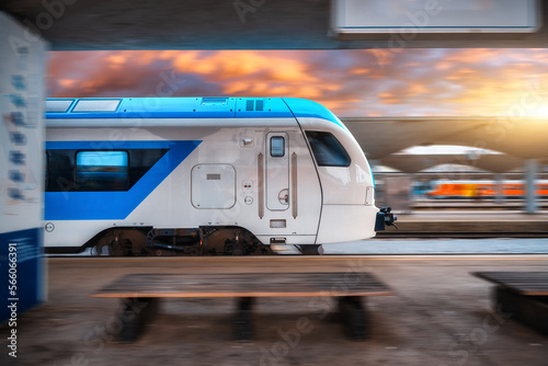 Blue high speed train in motion on the railway station at sunset. Fast modern intercity train and blurred background. Railway platform. Railroad. Commercial and passenger transportation. Side view
