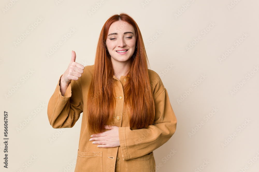 Young red hair woman isolated touches tummy, smiles gently, eating and satisfaction concept.