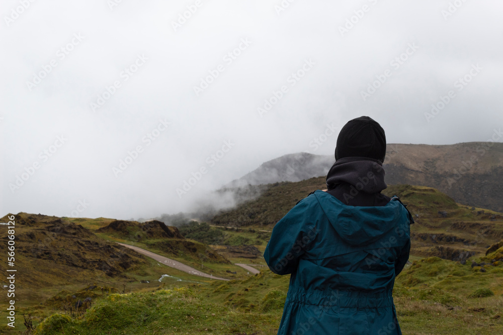 Young relax woman watching colombian paramo foggy landscape with grass mountains  and a sand road