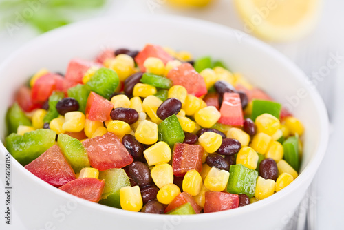 Mexican style colorful fresh vegetable salad made of beans  corn  tomato and green bell pepper served in white bowl  photographed on white wood  Selective Focus  Focus one third into the salad 